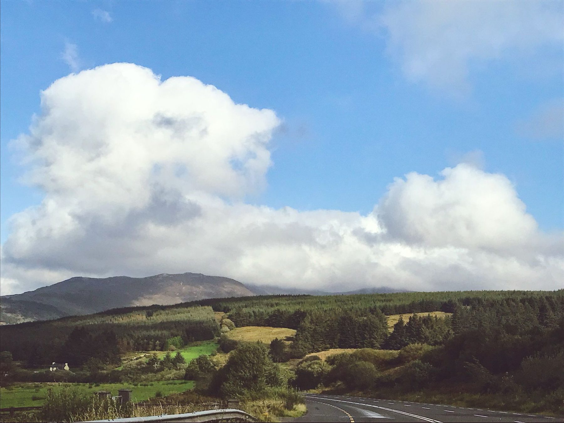 Open countryside road under a vast Irish sky — mountains and clouds